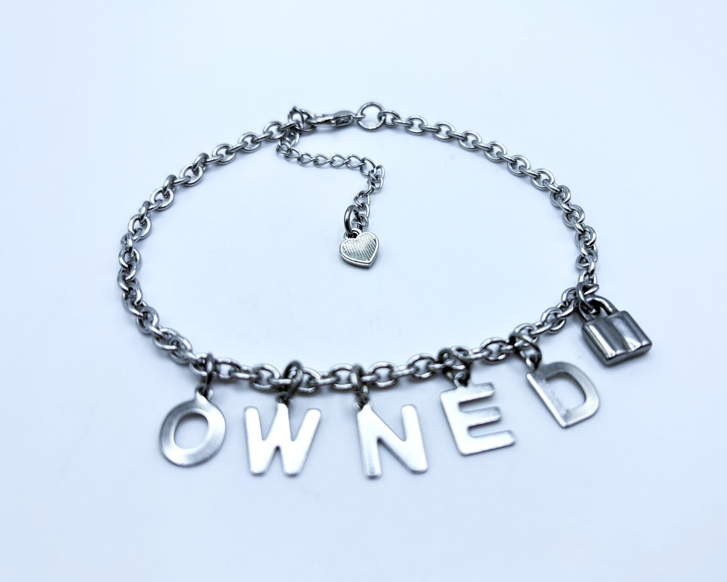 Silver chain bracelet with 'OWNED' charms on a light blue background
