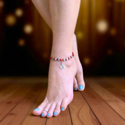 Person wearing a red beaded anklet on a wooden floor with a blurred background