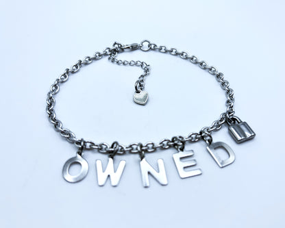 Silver chain bracelet with 'OWNED' charms on a light blue background