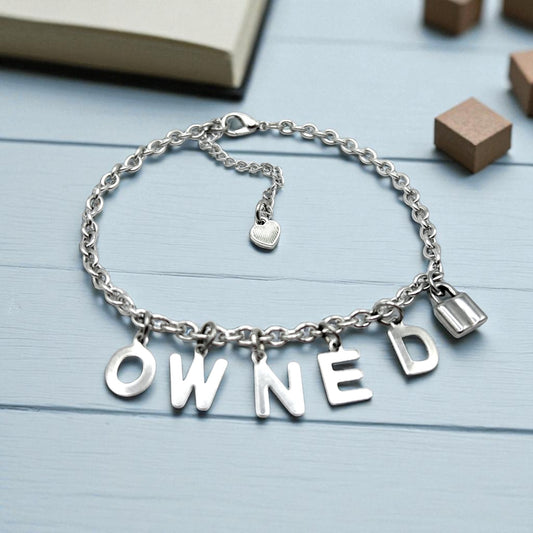 Silver bracelet with 'OWNED' charms on a light blue wooden surface